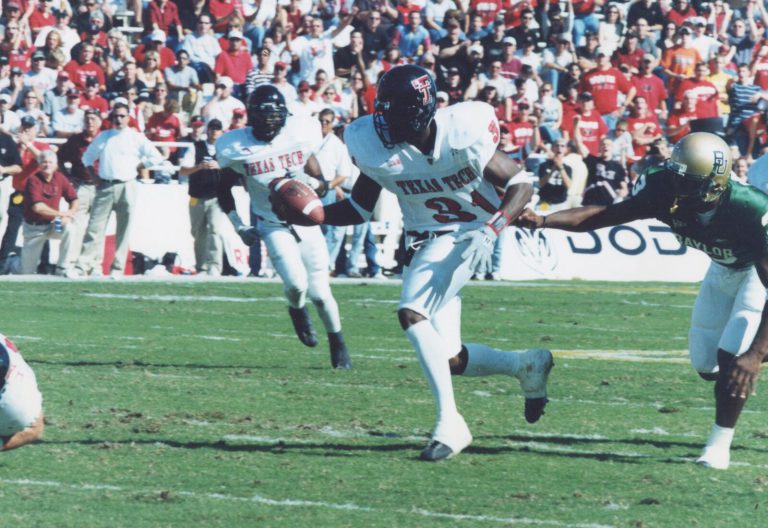 Kevin Curtis, number 31 in a white Texas Tech uniform, carrying the ball as a Baylor defender lunges from the side