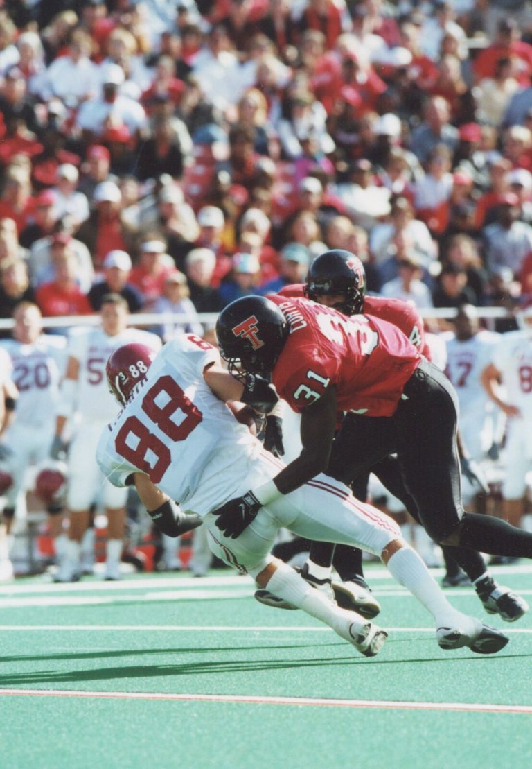 Kevin Curtis in a red number 31 Texas Tech jersey tackling a receiver in a white number 88 jersey