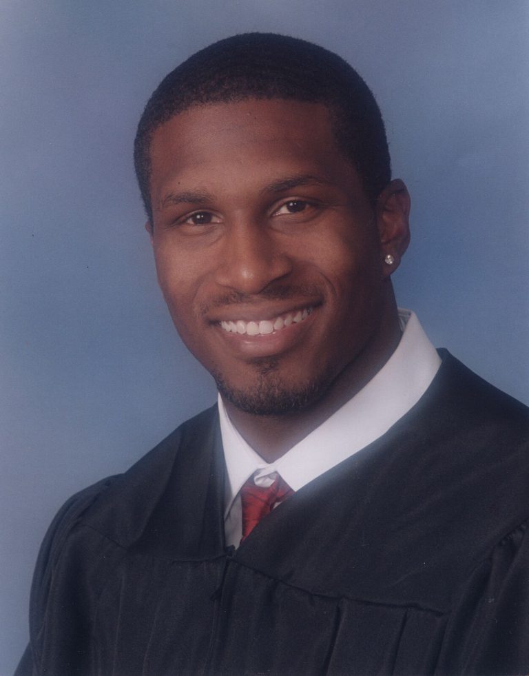 Kevin Curtis smiling in a formal studio portrait, wearing a black robe and red tie