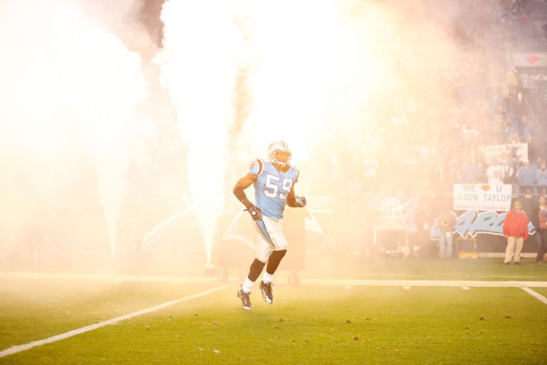 Landon Johnson, No. 59 in a light blue Panthers jersey, running through smoke onto the field before a game
