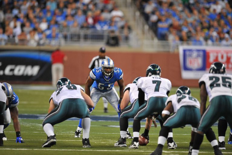 Landon Johnson, No. 55 in a blue Lions jersey, facing an offense in white and green at the line of scrimmage