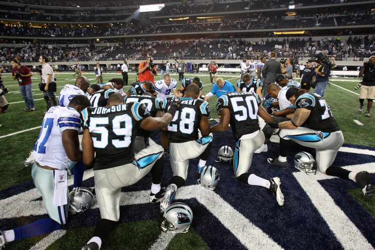 Landon Johnson, No. 59 for the Panthers, kneeling in a prayer circle with Cowboys players at midfield