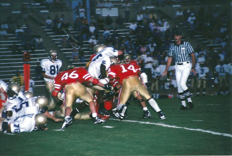 Landon Johnson in a red No. 14 jersey with teammates stopping a ball carrier in a high school game
