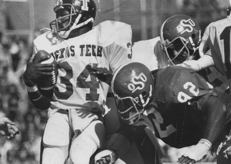 Larry Isaac in a white Texas Tech number 34 jersey clutching the ball as two defenders in OSU helmets close in