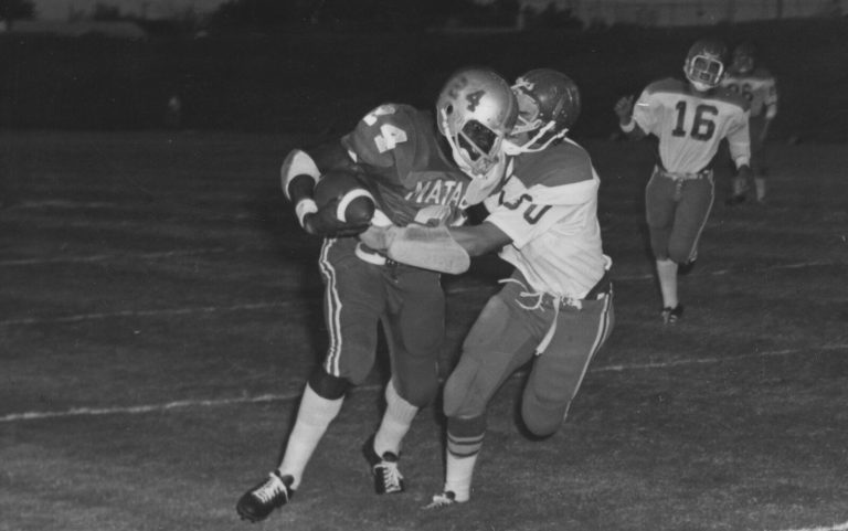 Larry Isaac in a Matadors jersey carrying the ball as a defender in a white jersey grabs for the tackle