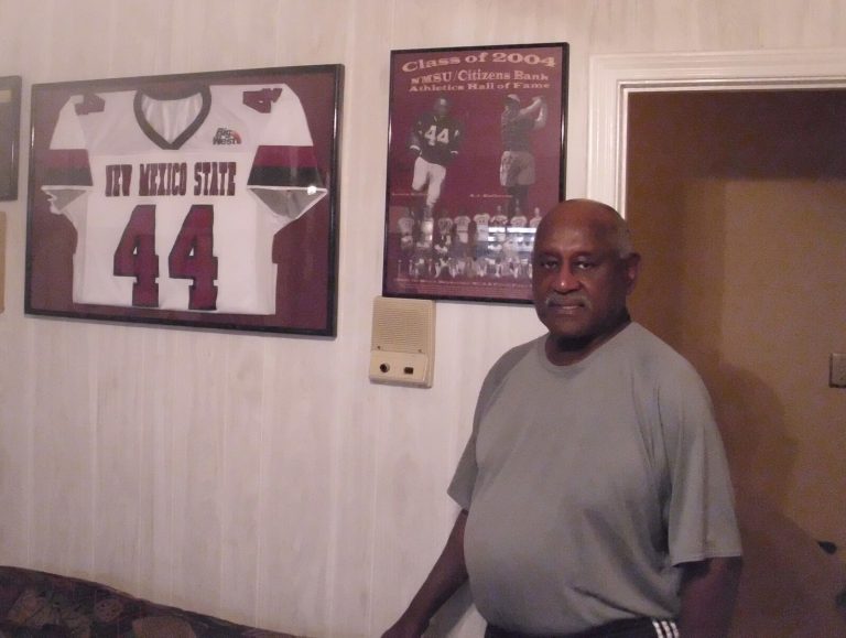 Louis Kelley beside a framed New Mexico State No. 44 jersey and a 2004 Athletics Hall of Fame poster