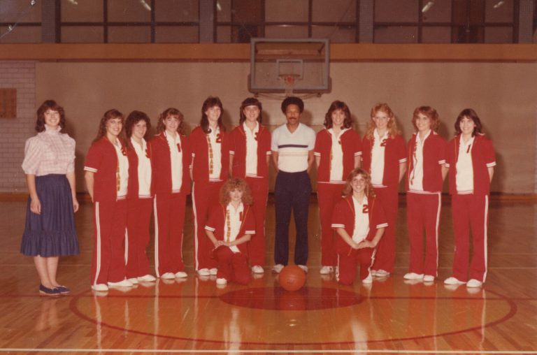 Melvin Houston with a girls team in red warm-ups posed on a gym floor, vintage color team photo