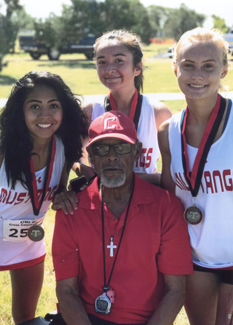 Melvin Houston seated in a red polo with three Mustangs runners wearing medals