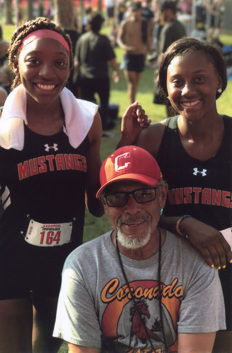 Melvin Houston in a Coronado shirt and red cap seated in front of two smiling Mustangs runners