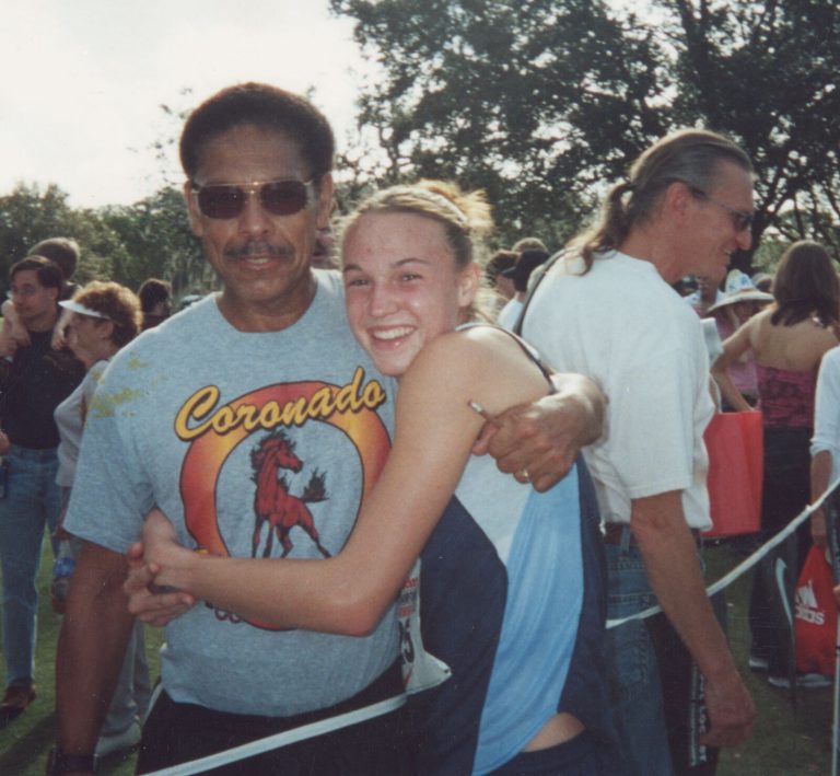 Melvin Houston in sunglasses and a Coronado T-shirt hugging a smiling runner at a meet