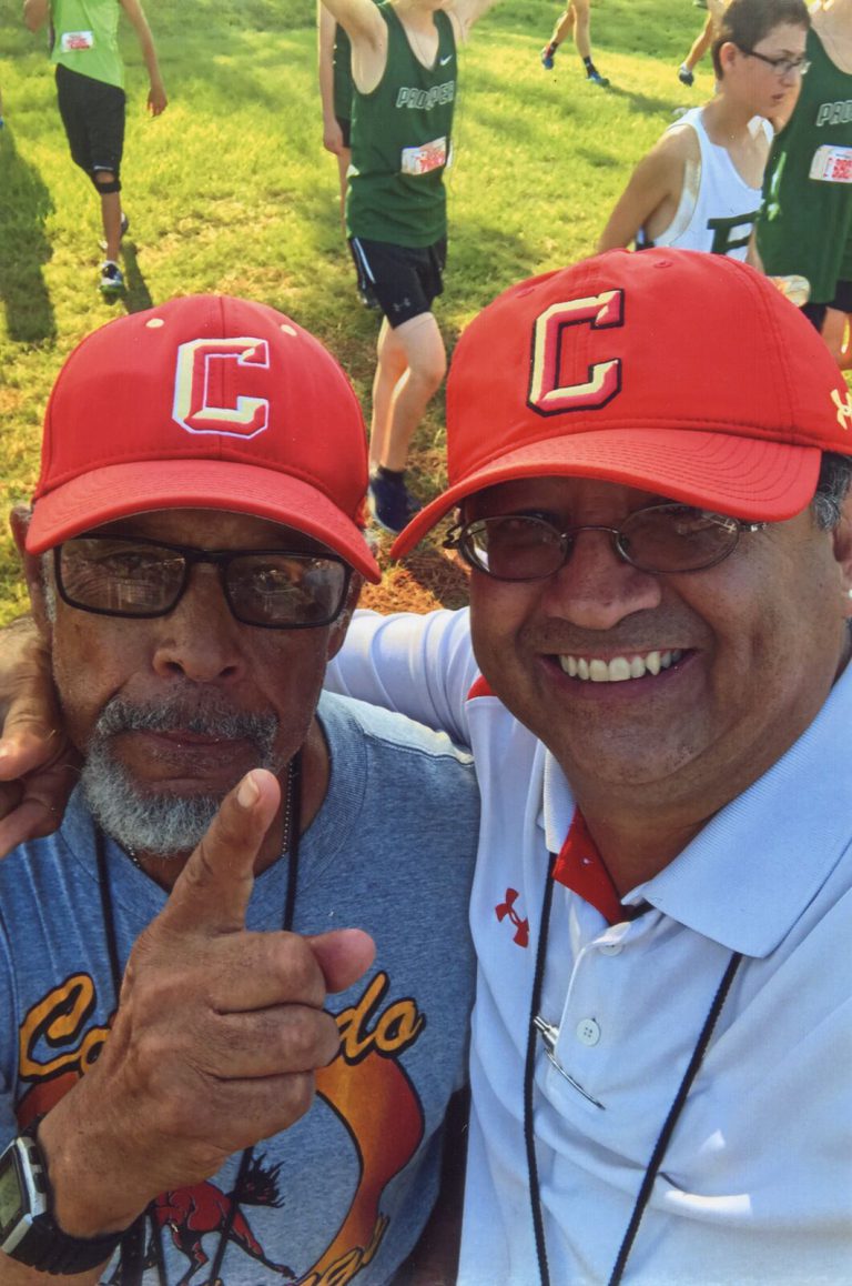 Melvin Houston and another man in matching red Coronado caps smiling for a selfie outdoors
