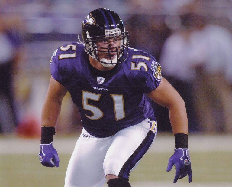 Mike Smith in a purple number 51 Baltimore Ravens jersey and black helmet, crouched ready on the field