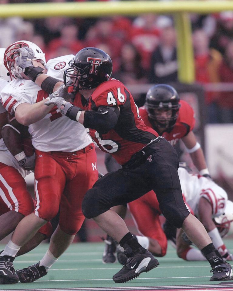 Mike Smith, number 46 in a red and black Texas Tech uniform, pushing past a blocker in a white jersey