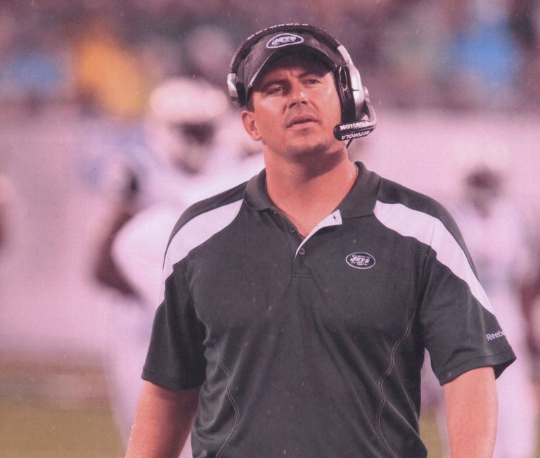 Mike Smith in a New York Jets polo and headset watching from the sideline in the rain