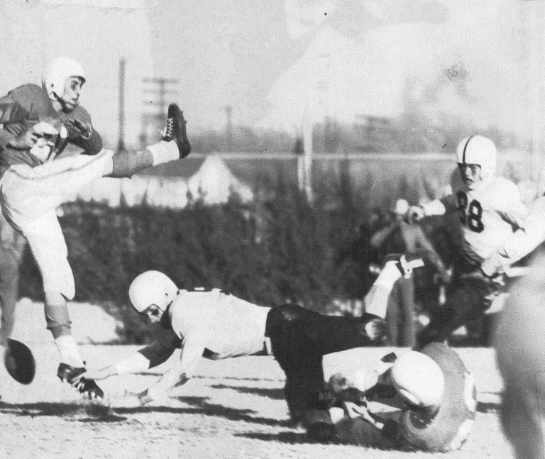 Pat Hartsfield, number 88, in a white jersey as a kicker boots the ball and players dive for it