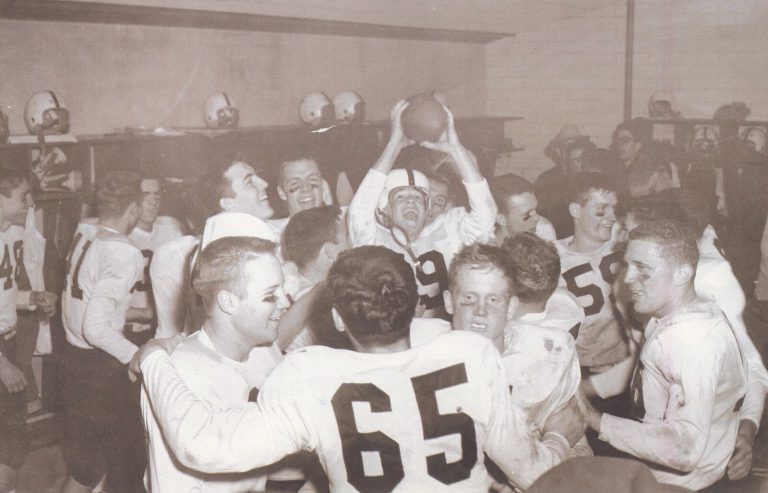 Pat Hartsfield's football team celebrating in a locker room as one player holds up the ball