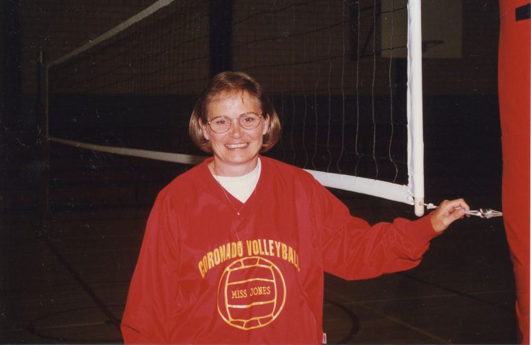 Patty Jones in a red Coronado Volleyball pullover reading Miss Jones, smiling beside a volleyball net