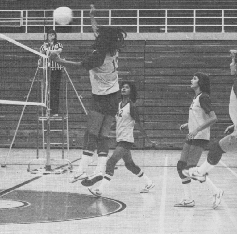 Volleyball hitter leaping at the net as a referee watches, from a Coronado district title clipping, Patty Jones collection