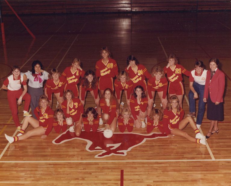 Patty Jones's 1983 Coronado Mustangs JV volleyball team posed on the gym floor around a Mustang logo