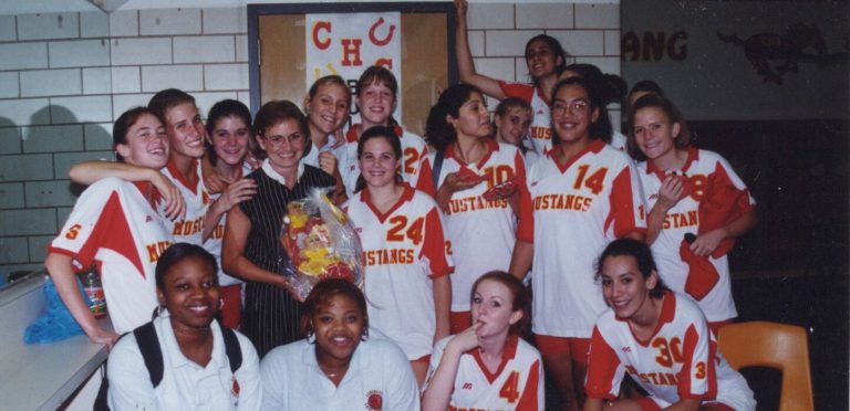 Coronado volleyball players celebrating around a smiling woman in glasses holding a gift basket, Patty Jones collection