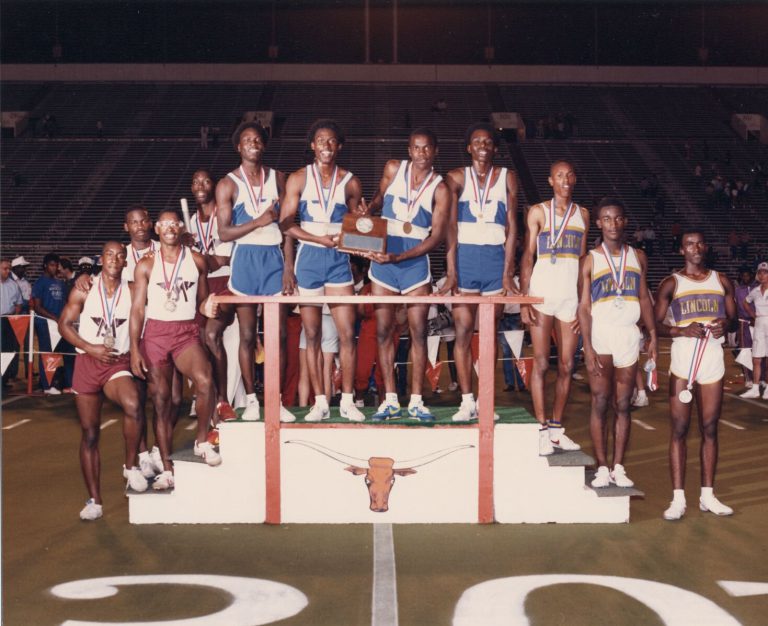 Relay runners in blue and white holding a plaque at center of a Longhorn podium, from Percy Hines' collection