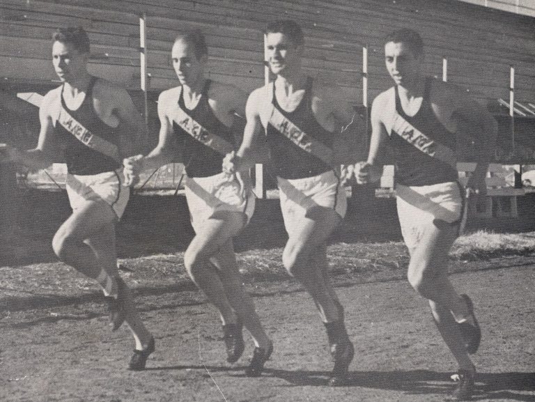 Four relay runners in sashed track uniforms mid-stride, black-and-white photo from the Pete Ragus collection