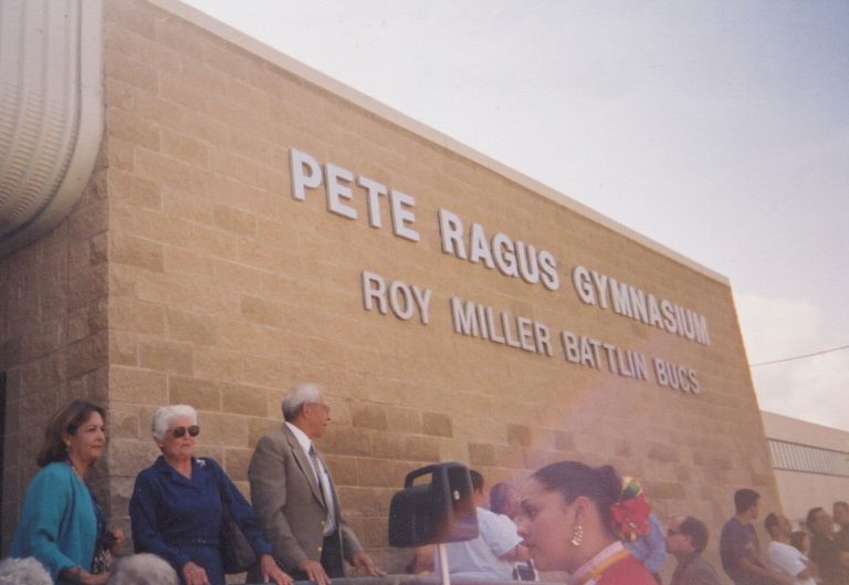 Guests gathered outdoors beneath wall lettering that reads Pete Ragus Gymnasium, Roy Miller Battlin Bucs