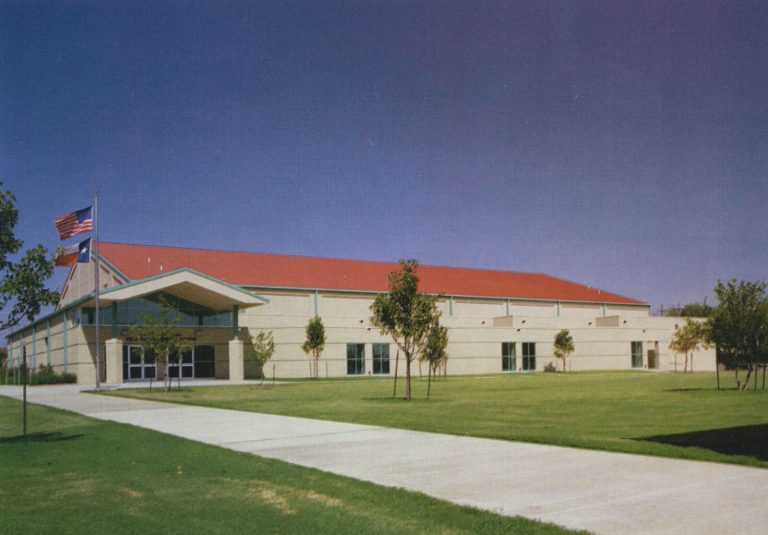 Pete Ragus Aquatic Center building with a red roof and American and Texas flags out front