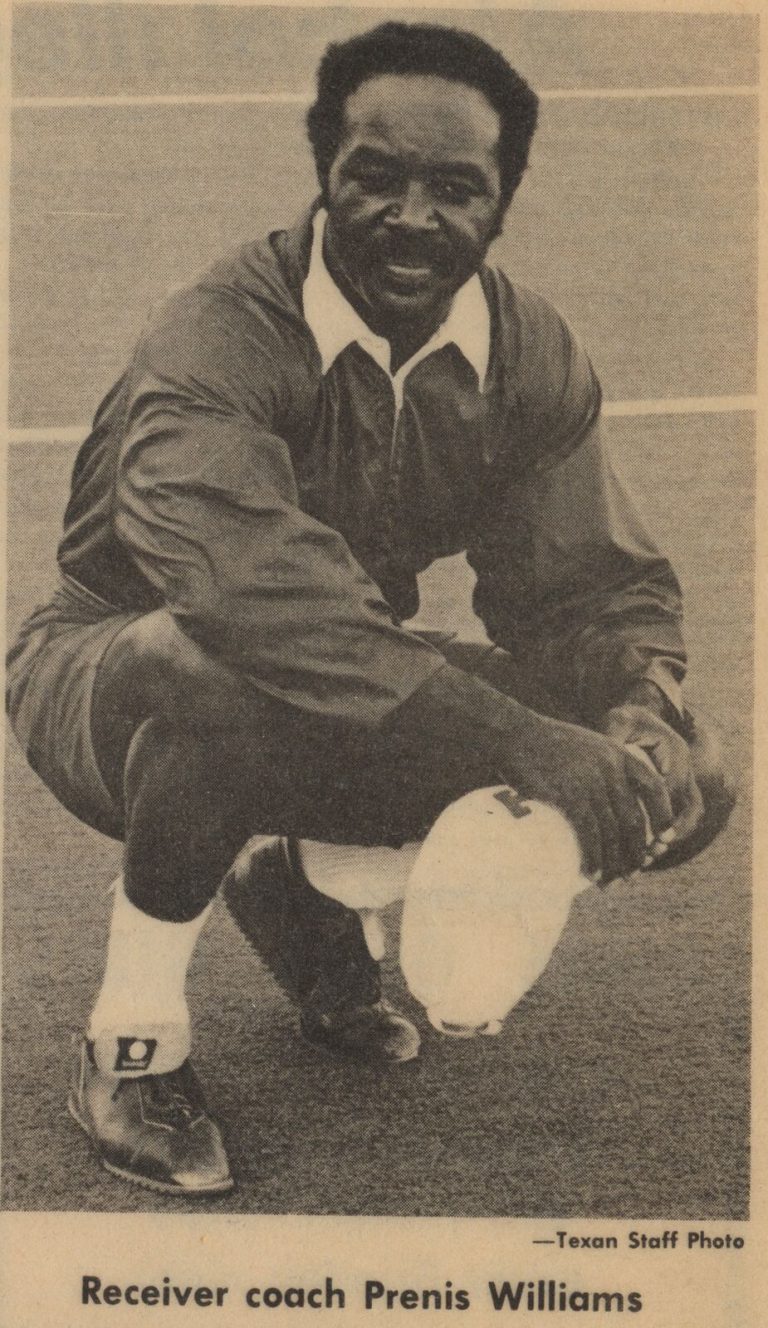 Prenis Williams, Texas receiver coach, crouching on the field beside a helmet, from a Daily Texan photo