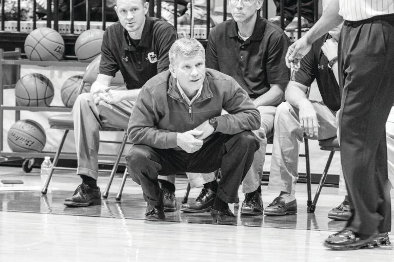Randy Dean with fellow Coronado coaches on the bench during a game, black and white