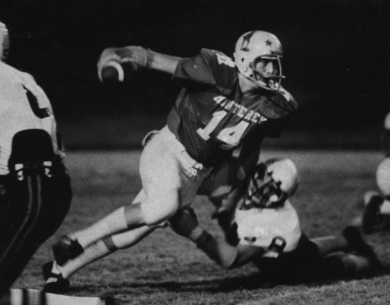 Ron Reeves in a Monterey number 14 jersey scrambling with the ball cocked to throw during a night game