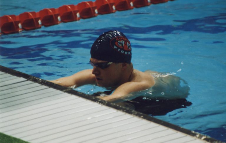 Thomas Klement in an Auburn Tigers swim cap and goggles resting at the edge of a pool