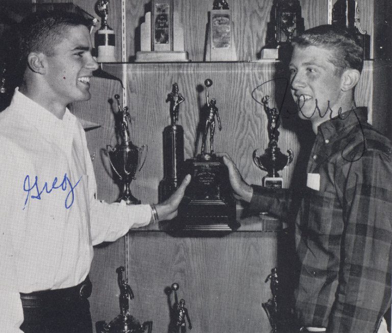 Greg Lott, left, with a classmate at a trophy case, black and white