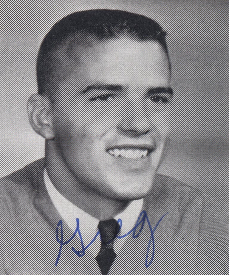 Greg Lott smiling in a sweater and tie, signed black-and-white portrait
