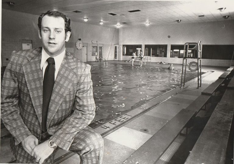 Ron Holihan in a plaid suit seated at the edge of the Lorain Family YMCA pool, early in an aquatics career