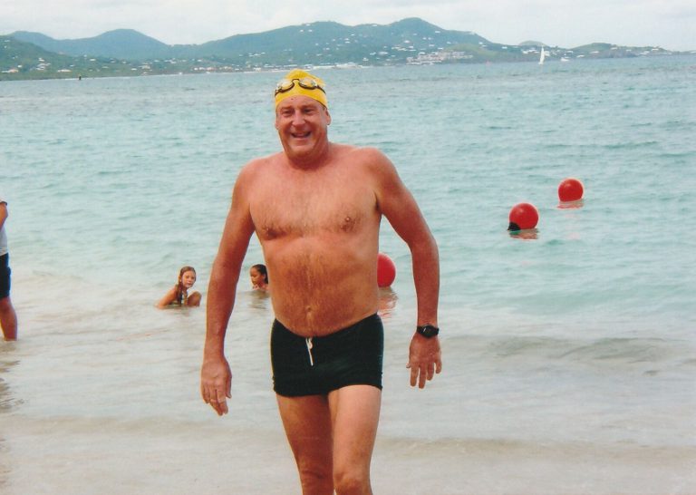 Ron Holihan in a yellow swim cap walking out of the water after finishing the 12th St. Croix five-mile ocean swim