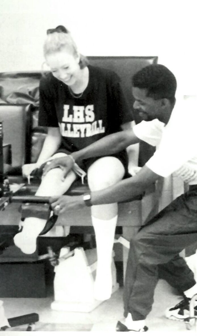 Athletic trainer taping a volleyball player's leg in an LHS Volleyball shirt, from the Anthony Peppers collection