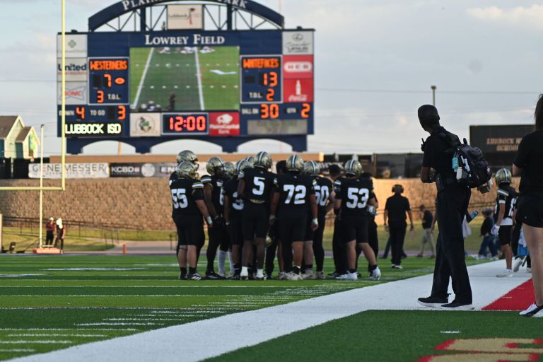 Lubbock High sideline at Lowrey Field with players in a huddle under the scoreboard, from the Anthony Peppers collection