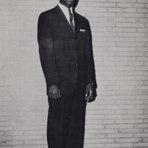 Joe McWilliams stands in a suit and tie in front of a brick wall in a vintage Dunbar High School photo.