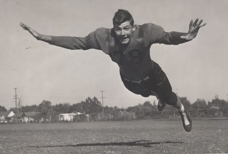 Mac Taylor flying through the air with arms outstretched on a football field