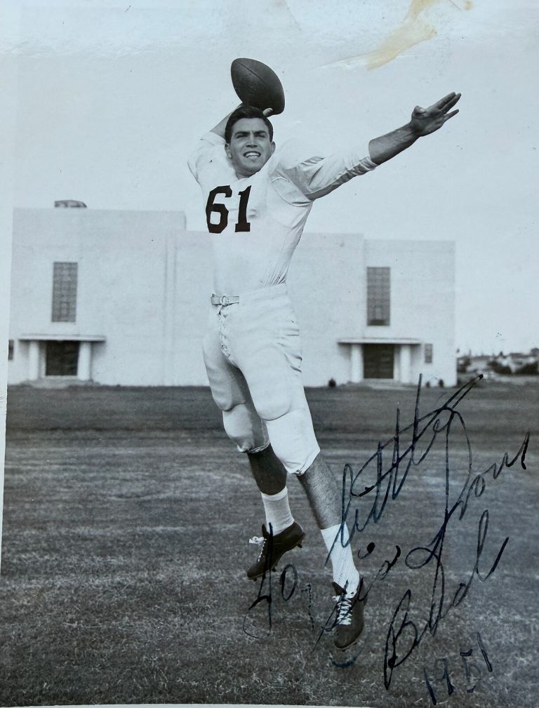 Mac Taylor in a white number 61 jersey leaping with a football, an autographed print