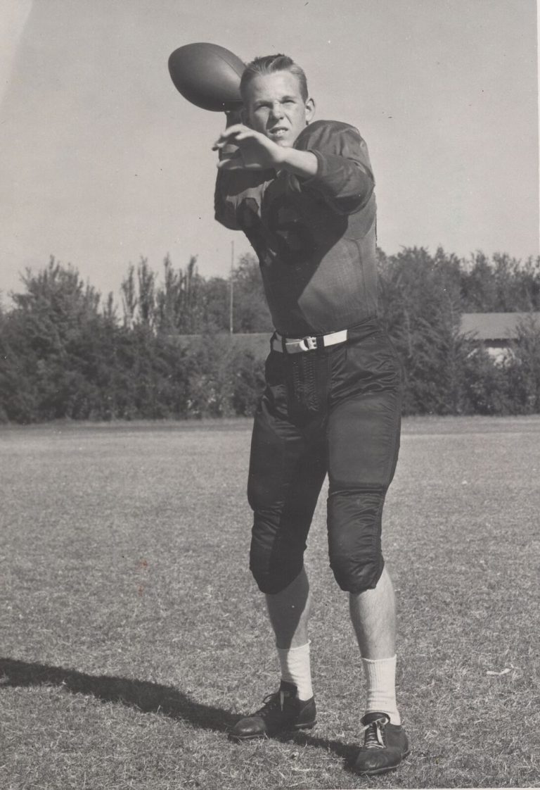 Mac Taylor winding up to throw a football on a grass field
