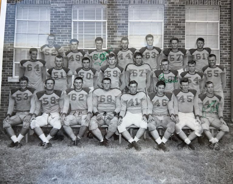 Westerners football team posed in three rows in front of a brick building, 1950s team photo from the Mac Taylor scrapbook