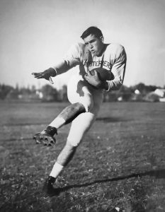 Mac Taylor in his Lubbock High Westerners uniform striking a kicking pose with the football, around 1950