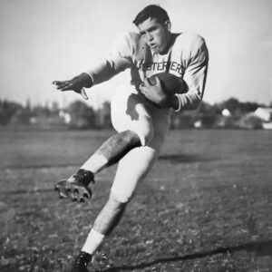 Mac Taylor in his Lubbock High Westerners uniform striking a kicking pose with the football, around 1950