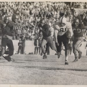 Mac Taylor, number 61, carries the ball past defenders in front of a packed stadium crowd around 1950