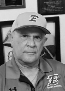 Robert "Prof" Ramos in an Estacado cap and Sports Medicine polo with his award plaques on the wall behind him.