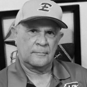 Robert "Prof" Ramos in an Estacado cap and Sports Medicine polo with his award plaques on the wall behind him.
