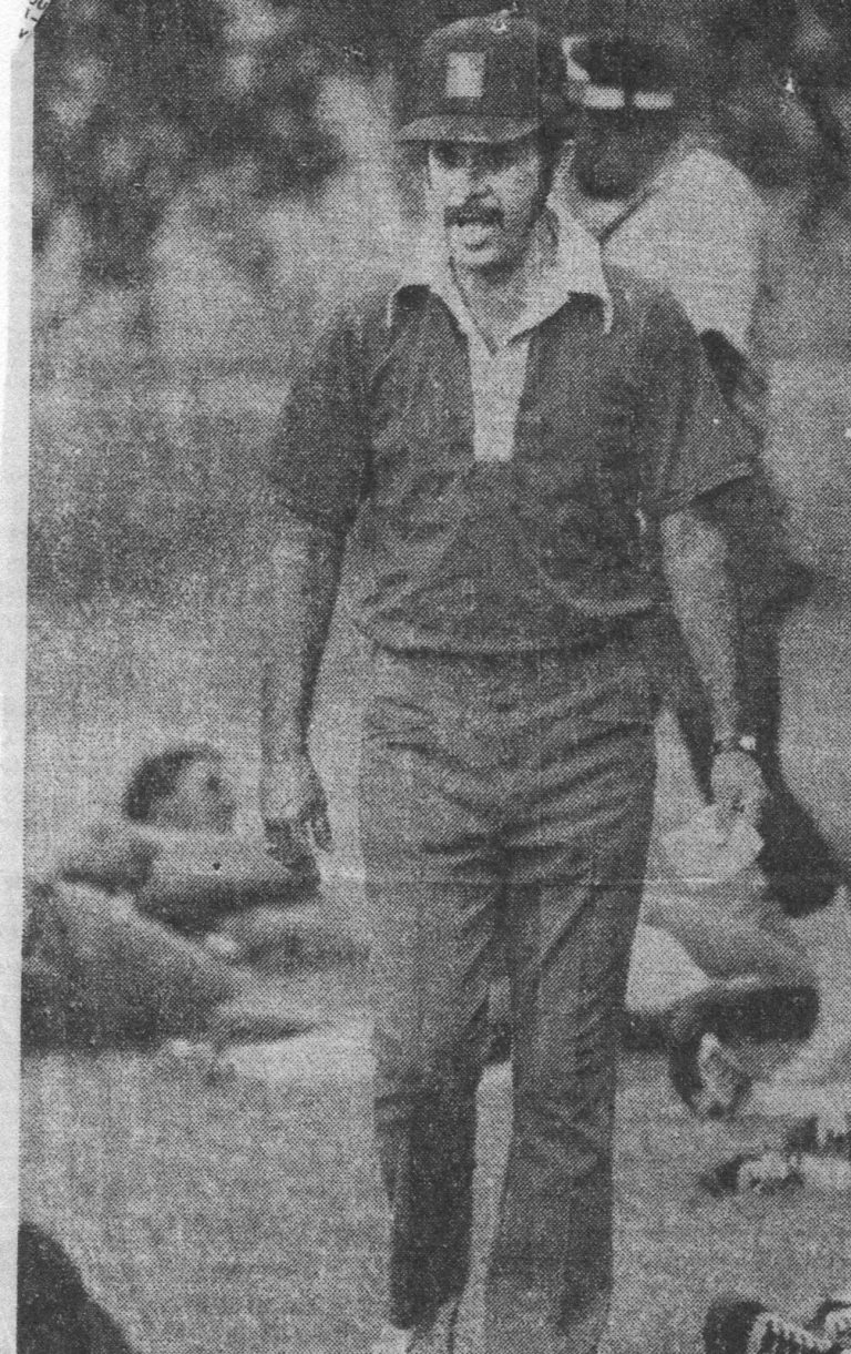 Robert “Prof” Ramos in a cap and collared shirt on the field with players on the ground nearby, from a newspaper clipping