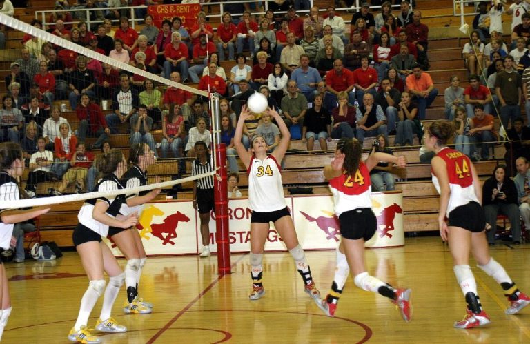 Robyn Smith Everson in a white number 34 jersey setting the ball at the net before a packed gym
